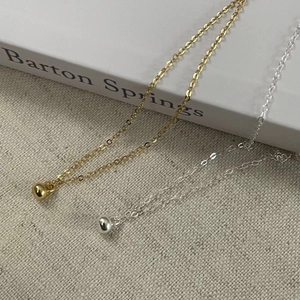 Detail of minimalist gold and silver bean pendants on fine chains over a textured fabric