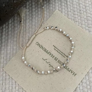 Vue détaillée d'un bracelet tissé beige avec perles argentées facettées et pompons