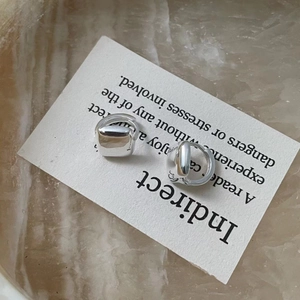 Macro detail of silver geometric square hoop earrings resting on a white card background