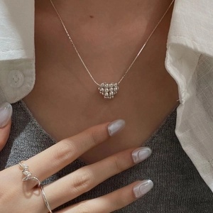 Gros plan du collier coeur en argent S925 et de la bague en perles sur tricot gris chic