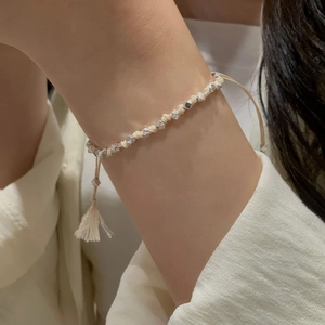 Détail d'un bracelet en coton beige tissé à la main avec perles argentées et pompons
