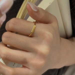 Close-up of a minimalist golden ring with a matte rectangular bar on a hand over a book