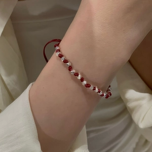 Gros plan d'un bracelet tressé rouge avec des perles d'argent facettées au poignet