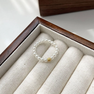 Macro detail of elastic pearl ring with gold bead in a velvet jewelry display box