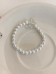 Close-up of S925 silver beaded bracelet with faux pearls and a bow charm on a ceramic tray