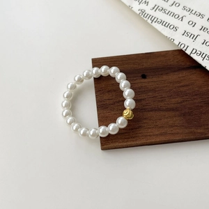 Elastic S925 silver pearl ring with a textured gold bead on a minimalist wooden base