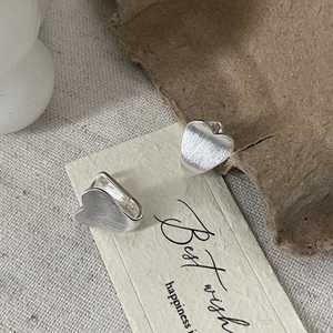 Minimalist S925 sterling silver heart studs with brushed texture on a warm fabric background