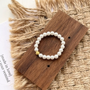 Elastic S925 silver pearl ring featuring a textured gold bead on a rustic wooden base