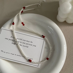 Collier élégant en argent S925 avec nœud et perles blanches et rouges sur un plat en céramique