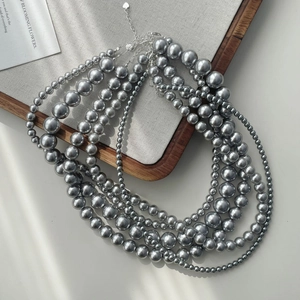 Detail of layered silver-grey faux pearl necklaces with heart clasp on wooden tray