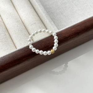 Detail of elegant S925 silver pearl elastic ring with a single golden bead accent