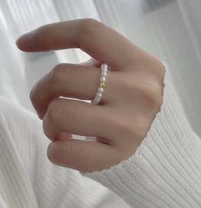 Detailed view of an elastic pearl bead ring with a central gold accent on a finger