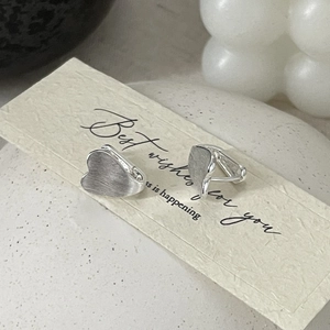 Detail showing brushed silver heart earrings on decorative card with soft aesthetic lighting