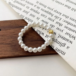 Detail of s925 silver elastic pearl ring with a textured gold bead on a wooden prop