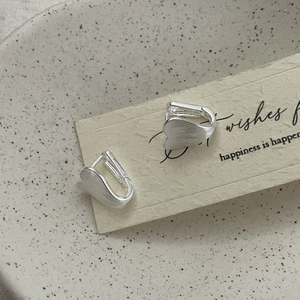 Macro detail of silver S-shaped stud earrings with brushed matte texture on card