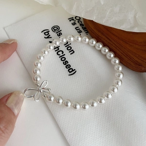 Detail of elegant S925 silver bow pendant and glossy cream pearls on the stylish bracelet