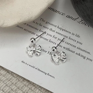 Macro shot of polished silver bow stud earrings resting on artistic white paper