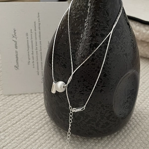 Détail d'un collier en argent avec pendentif sphère brossée sur un vase noir