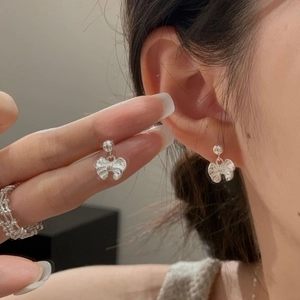 Detailed view of elegant silver bow earrings and a cutout chain ring worn by a model