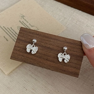 Detail of silver bow earrings with textured surface on a dark wood background