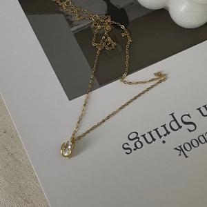 Close-up of golden teardrop pendant with clear faceted crystal on a fine link chain