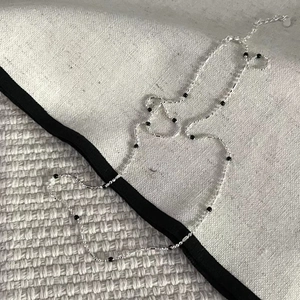 Detail of S925 sterling silver ball chain necklace with black beads on a textured fabric