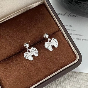Close-up of silver bow stud earrings resting on a brown velvet jewelry box liner