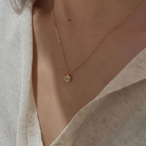 Close-up of minimalist gold oval zircon pendant necklace worn on a female model