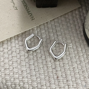 Detailed view of irregular U-shape silver earrings on a beige woven mat background