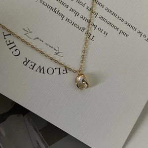 Detail of gold zircon necklace with an oval gemstone pendant on a decorative paper card