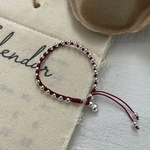 Detail of red braided cord bracelet with silver beads and small bell charm pendant