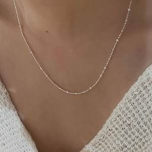 Detail of S925 sterling silver ball necklace worn by model on minimalist knitwear background