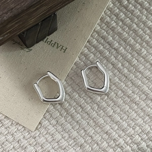 Macro shot of S925 silver irregular geometric huggie earrings on textured fabric