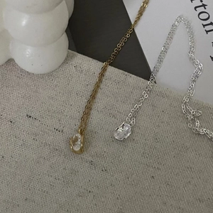 Detailed view of teardrop pendant necklaces in gold and silver on textured grey linen