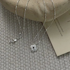 Detail of S925 silver necklace with black clover pendant on a rustic ceramic plate