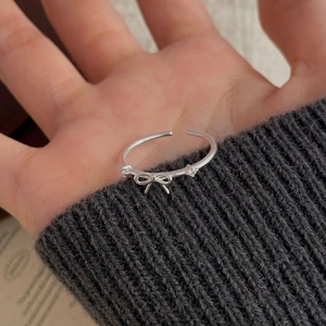 Détail d'une bague nœud en argent avec deux zircons sur fond de tricot gris chiné