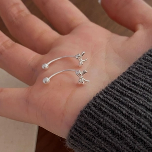 S925 silver bow stud earrings with curved bar held in hand showing compact size