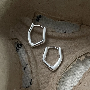 Detail view of silver S925 irregular geometric hoop earrings on textured fabric background
