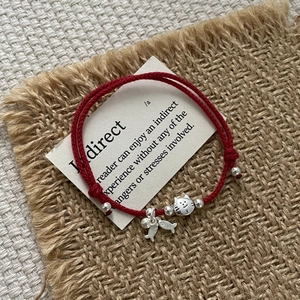 Detailed shot of red woven rope bracelet with silver cat and fish charms on rustic fabric