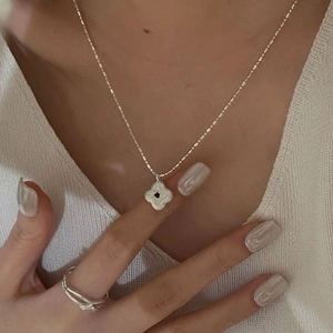 Close-up of S925 silver clover necklace with black gemstone and layered ring on model