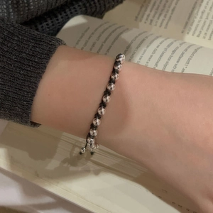 Detail shot of a silver bead bracelet with black woven cord on a wrist and book background