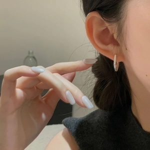 Macro side view of minimal polished silver hoop earring worn by a model in soft lighting