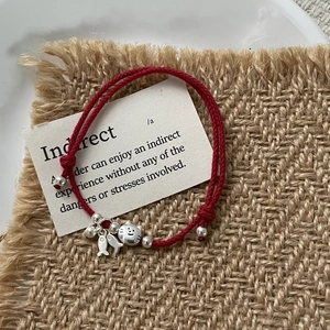 Close-up of red braided rope bracelet featuring silver cat and fish charms on burlap