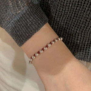 Detail of silver gourd bead bracelet with red woven cord on a female model wrist