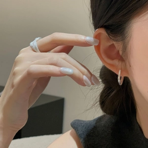 Close-up of minimalist silver irregular earrings and layered rings worn by a model