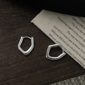 Detail of irregular pentagon S925 sterling silver hoop earring on vintage fabric texture