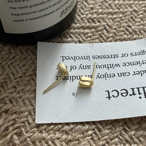Macro shot of minimalist matte gold U-shaped silver stud earrings on white card display