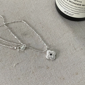 Macro detail of S925 silver four-leaf clover pendant with black gemstone on linen cloth