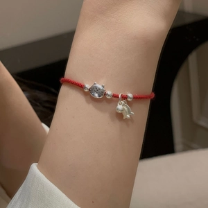 Detail of red woven string bracelet featuring a silver cat charm and bell on a wrist