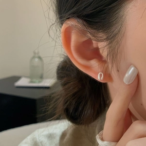 Minimalist white U-shaped stud earring worn on ear in a soft warm indoor lighting